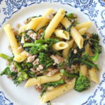 Penne pasta tossed with crumbed sausages and broccoli rabe on a white and blue dinner plate.