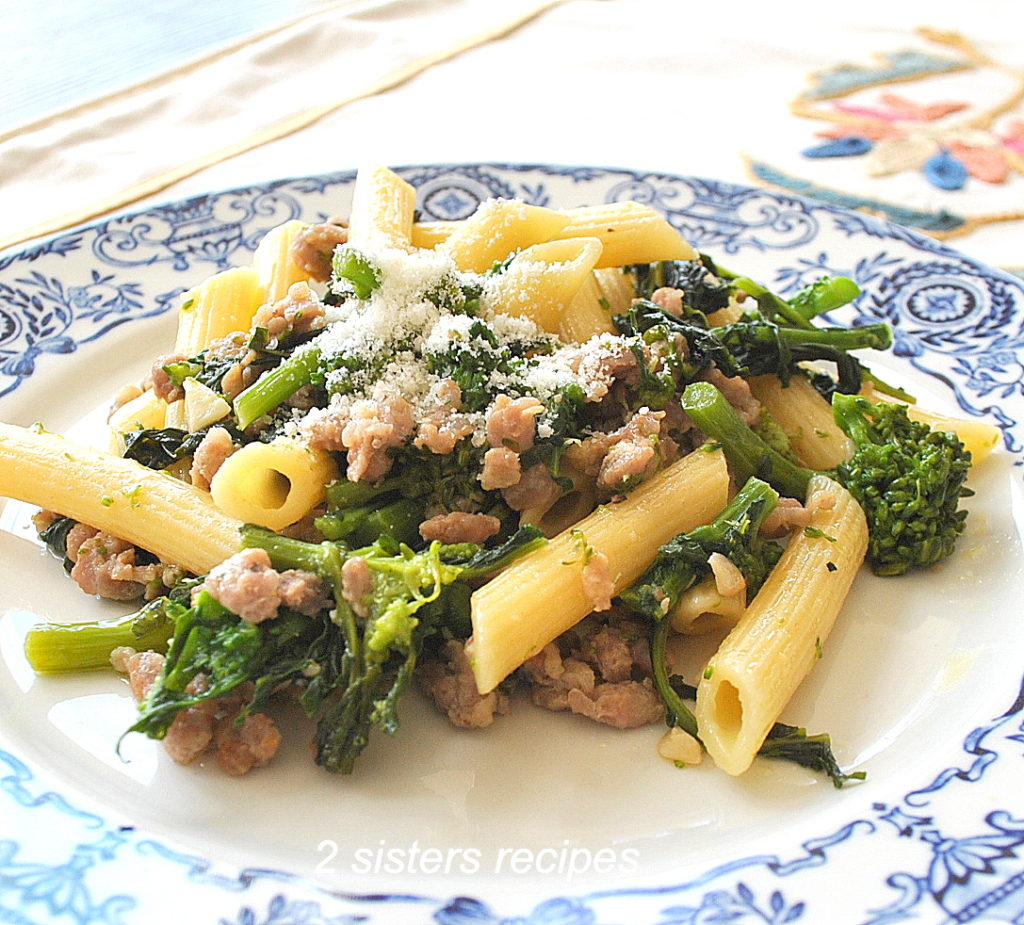 Penne pasta tossed with crumbled sausage and broccoli rabe on a white and blue plate. 