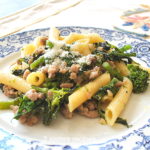Penne pasta tossed with crumbled sausage and broccoli rabe on a white and blue plate.
