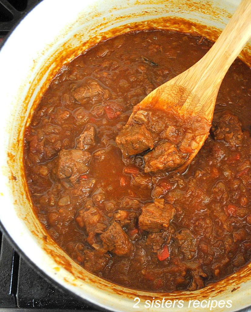 A large pot of beef stew stirred with a wooden spoon.