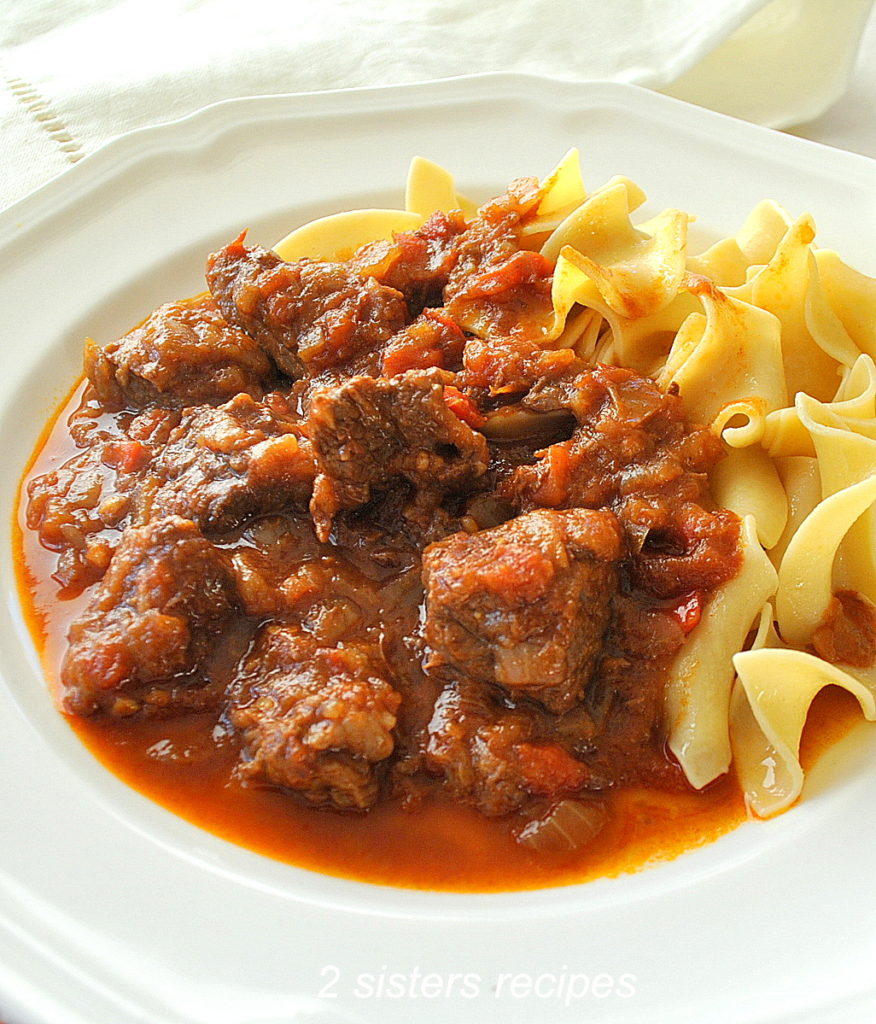 A white plate filled with a stew made with meat and a side of noodles. 
