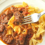 A forkful of of beef stew with wide noodles over a plate full of it.