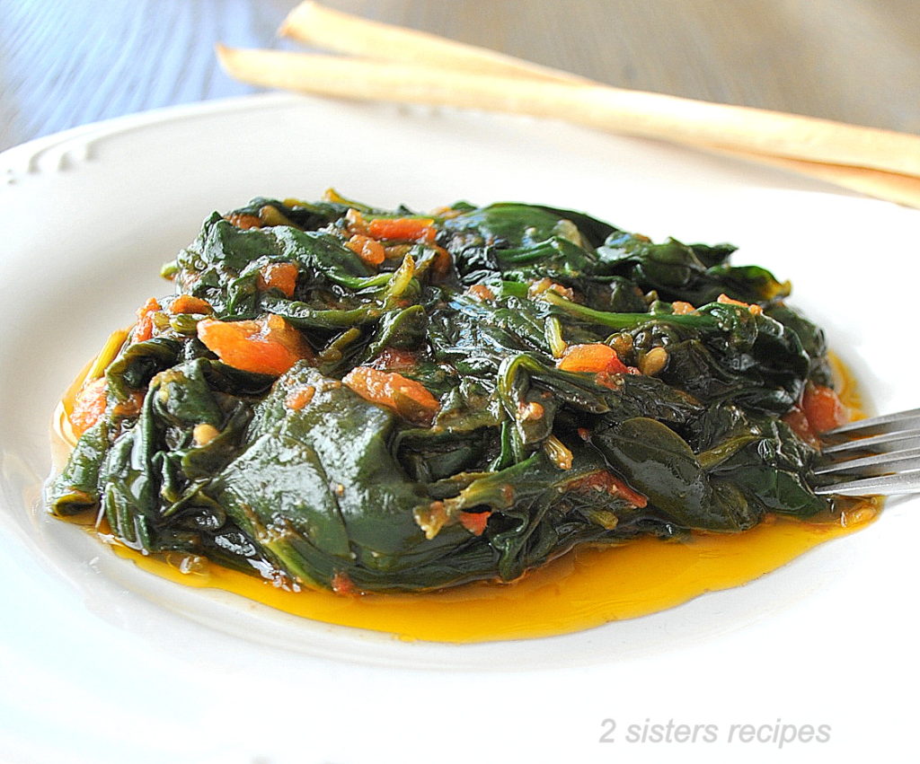 A white dish with some cooked spinach and Tomatoes. 