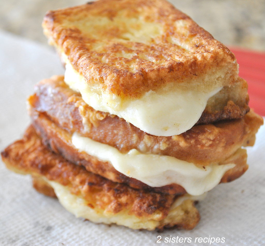 Three small crispy sandwiches with melted mozzarella in between piled on top of one another