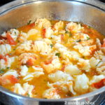 A large silver skillet filled with cooked lobster in a butter sauce.