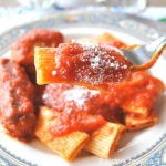 A forkful of rigatoni pasta with tomato sauce,a sausage links served on plate.