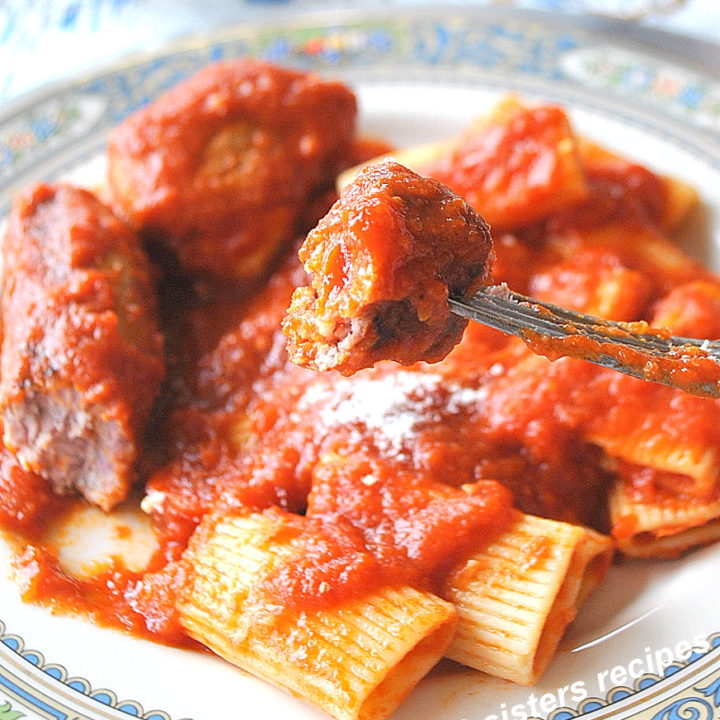 A forkful of sausage smothered in tomato sauce over a blue dinner plate.