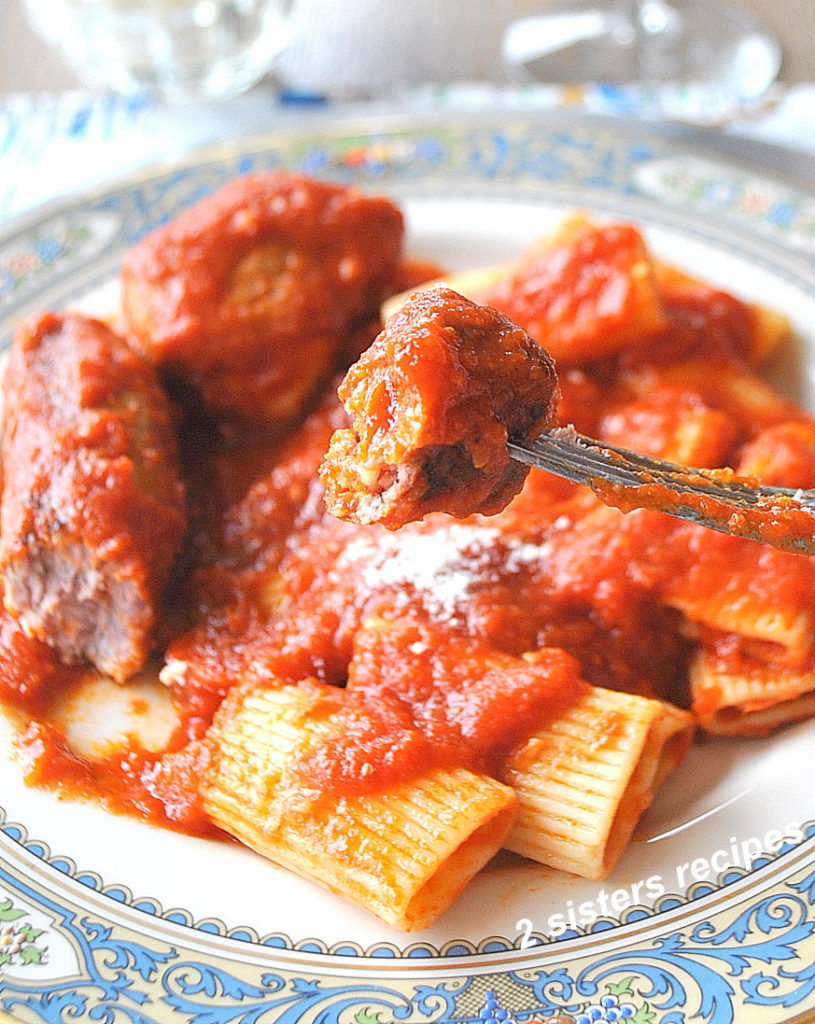 A forkful of sausage smothered in tomato sauce over a blue dinner plate.