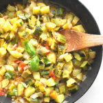 A large black skillet with our zucchini stew and a wooden spoon stirring.