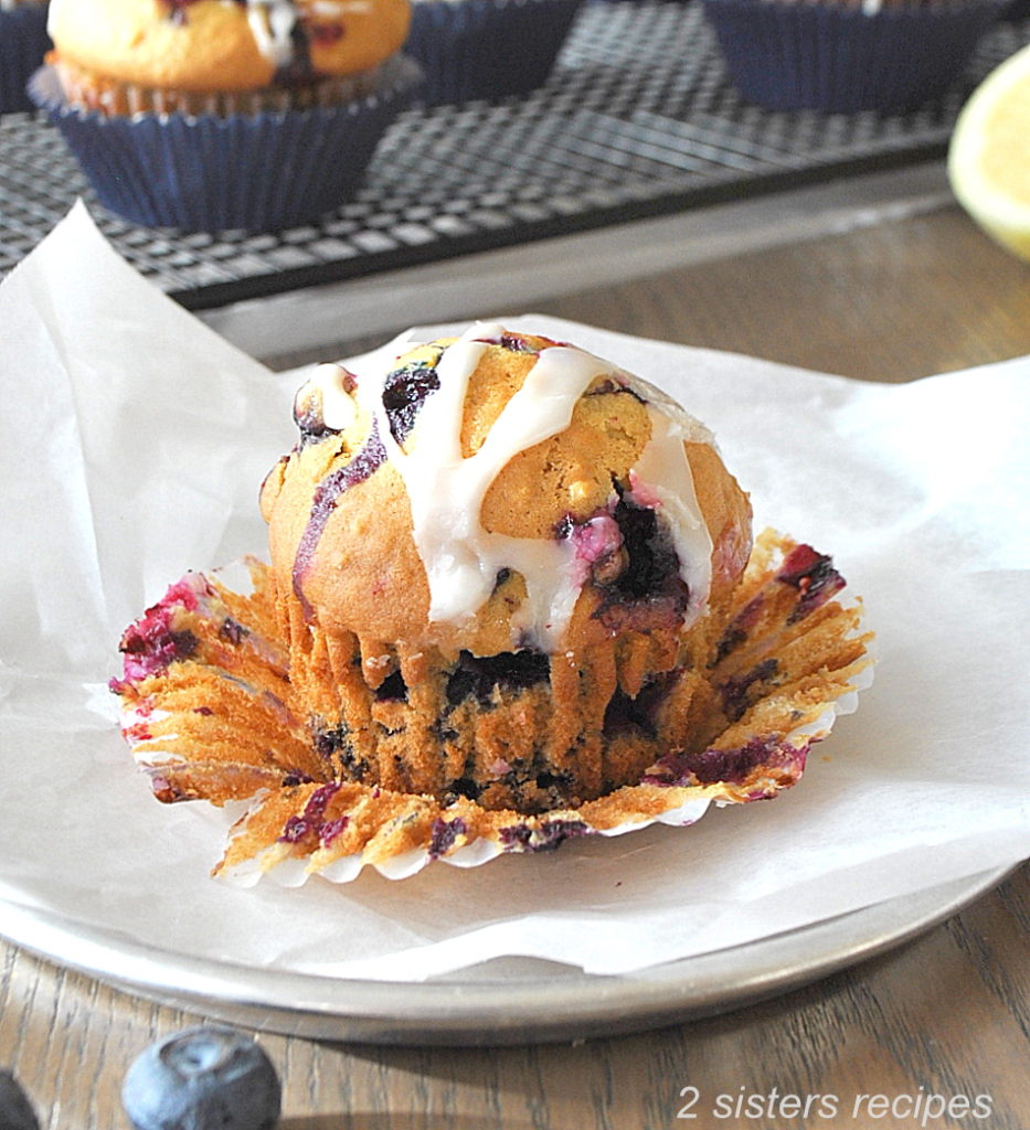 One baked Blueberry Muffin with the wrapper peeled off. by 2sistersrecipes.com