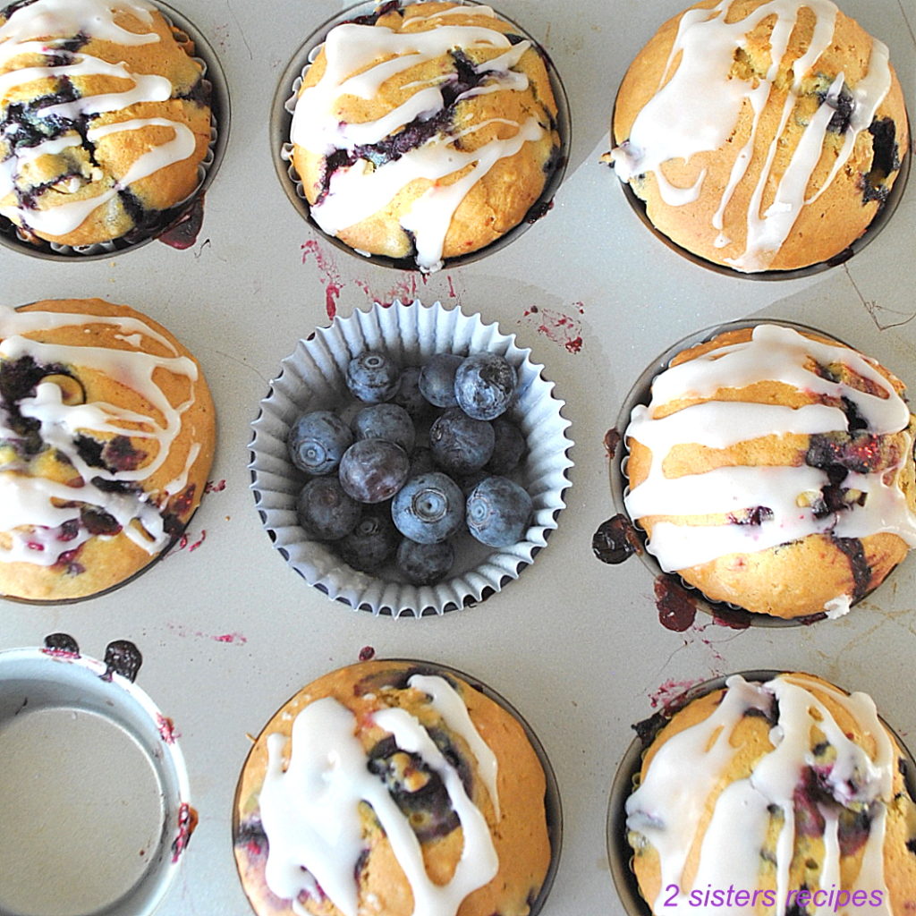 Blueberry lemon muffins inside a muffin pan with fresh blueberries in the center.