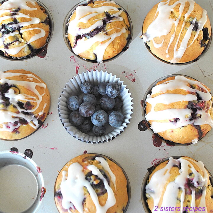 Blueberry lemon muffins inside a muffin pan with fresh blueberries in the center.
