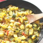 A large skillet with chopped zucchini stew and a wooden spoon.
