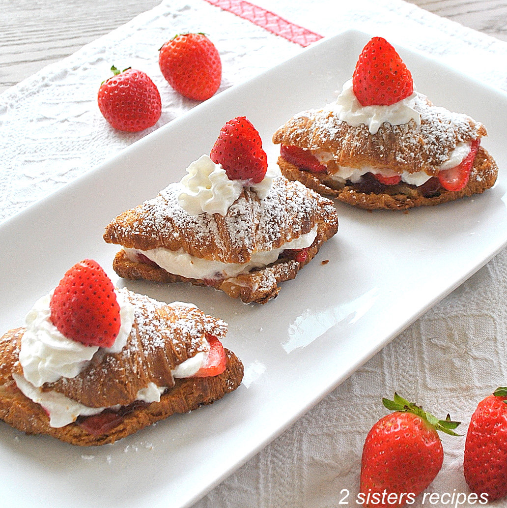 Easy Strawberry Shortcake Recipe A white platter with 3 small croissants filled with whipped cream and a fresh strawberry on top.