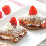 A white platter with two crossiants filled with whipped cream and a strawberry on top.