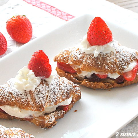 A white platter with two crossiants filled with whipped cream and a strawberry on top.