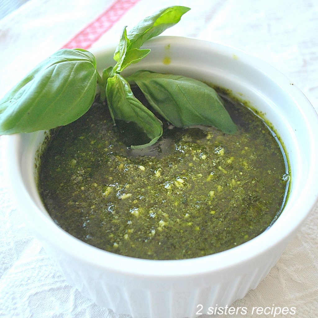 A white bowl filled with a spinach pesto sauce and fresh basil on the side.