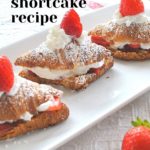 A white platter with 3 crossiants filled with whipped cream and strawberry on top.
