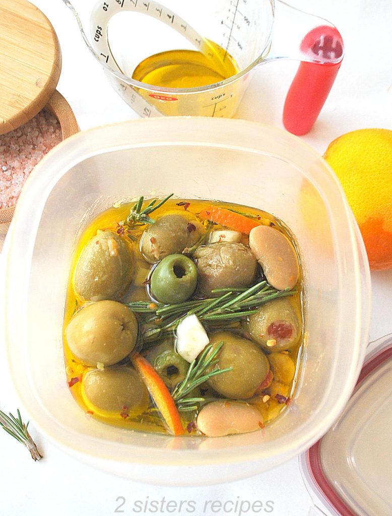Mixture of olive in olive oil inside a plastic container. by 2sistersrecipes.com