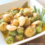 A square white bowl filled with marinated olives and beans.