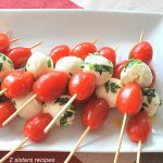 A white rectangular platter with skewers holding cherry tomatoes and small cheese balls.