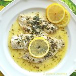 2 pieces of flounder fillets in Lemon Sauce and lemon slices served on a white plate.