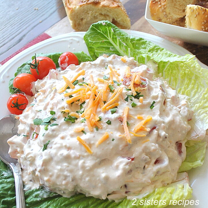 A large creamy dip topped with shredded cheddar and served on a bed of lettuce.