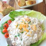 A white platter filled with a creamy dip, with shredded cheese on top and served on a bed of lettuce.