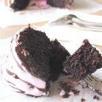 A forkful of chocolate cake with pink icing on top.