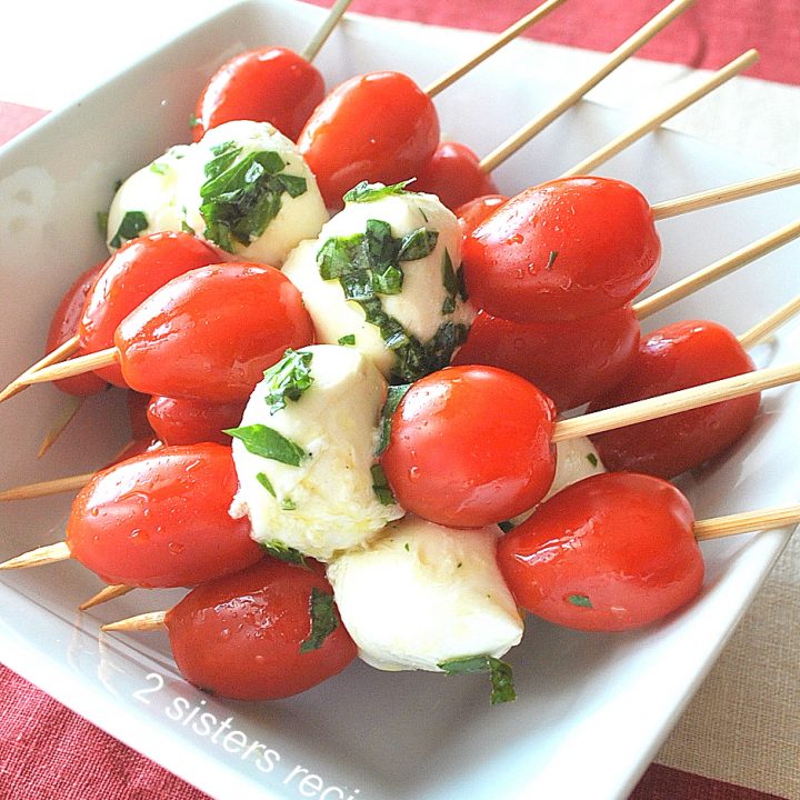 A white dish filled with cherry tomatoes and mozzarella balls on skewers.
