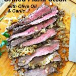 Grilled Flank Steak with caramelized onions sliced on a wood carving board.