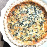 A white pie dish with a baked quiche filled with spinach and cheese.