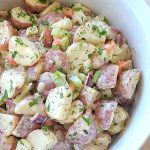 A white salad bowl filled with quartered red potatoes, veggies and fresh herbs.