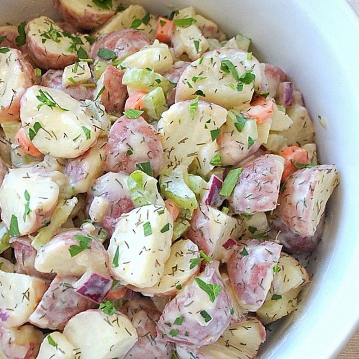 A white salad bowl filled with quartered red potatoes, veggies and fresh herbs.