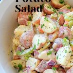 A white salad bowl filled with boiled cut potatoes, veggies and fresh herbs.