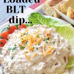 A creamy dip topped with shredded cheddar cheese is served on a bed of lettuce.