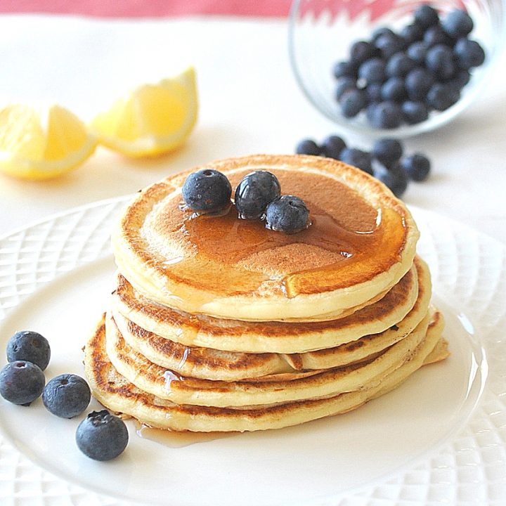 small pancakes piled on top in a white plate with blueberries on the side.
