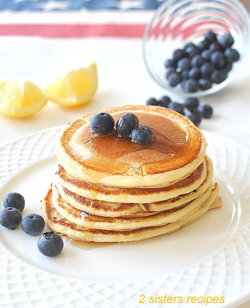  small pancakes piled on top in a white plate with blueberries on the side.