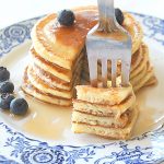 A forkful of lemon ricotta pancakes, with blueberries on top and on the side.