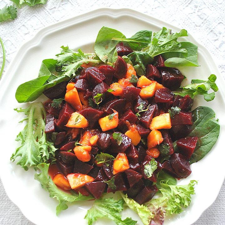 A white plate loaded with chopped beets and mango set on white plate with green lettuce.