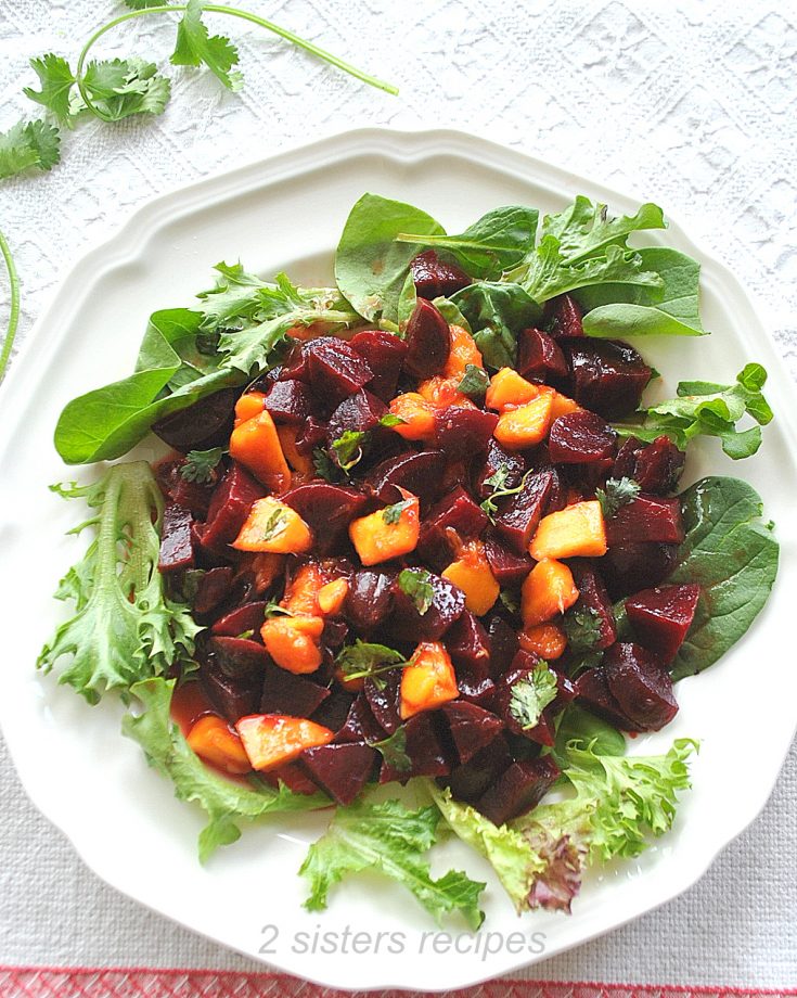 A white plate loaded with chopped beets and mango set on white plate with green lettuce.