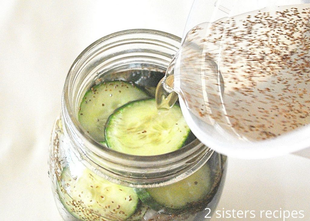 Pouring the liquid into the jar of cucumbers. by 2sistersrecipes.com 