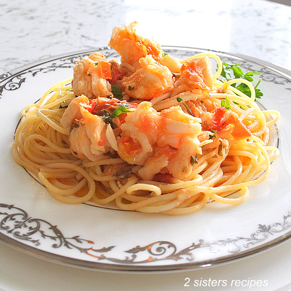 A white dinner plate with spaghetti and lobster meat and sauce on top.  by 2sistersrecipes.com