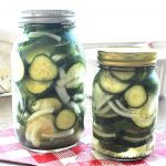 Two mason jars filled with sliced pickles, sliced onions, and liquid marinating.