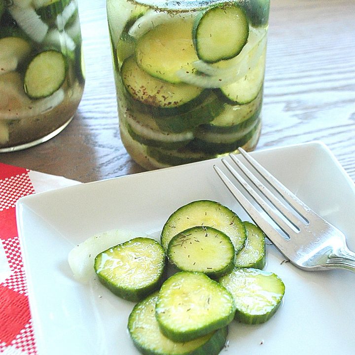 Two jars filled with pickles, and a white plate with a few pickles and a fork on the side.