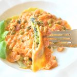 A forkful with spinach filled ravioli topped with a light cream tomato sauce and peas.