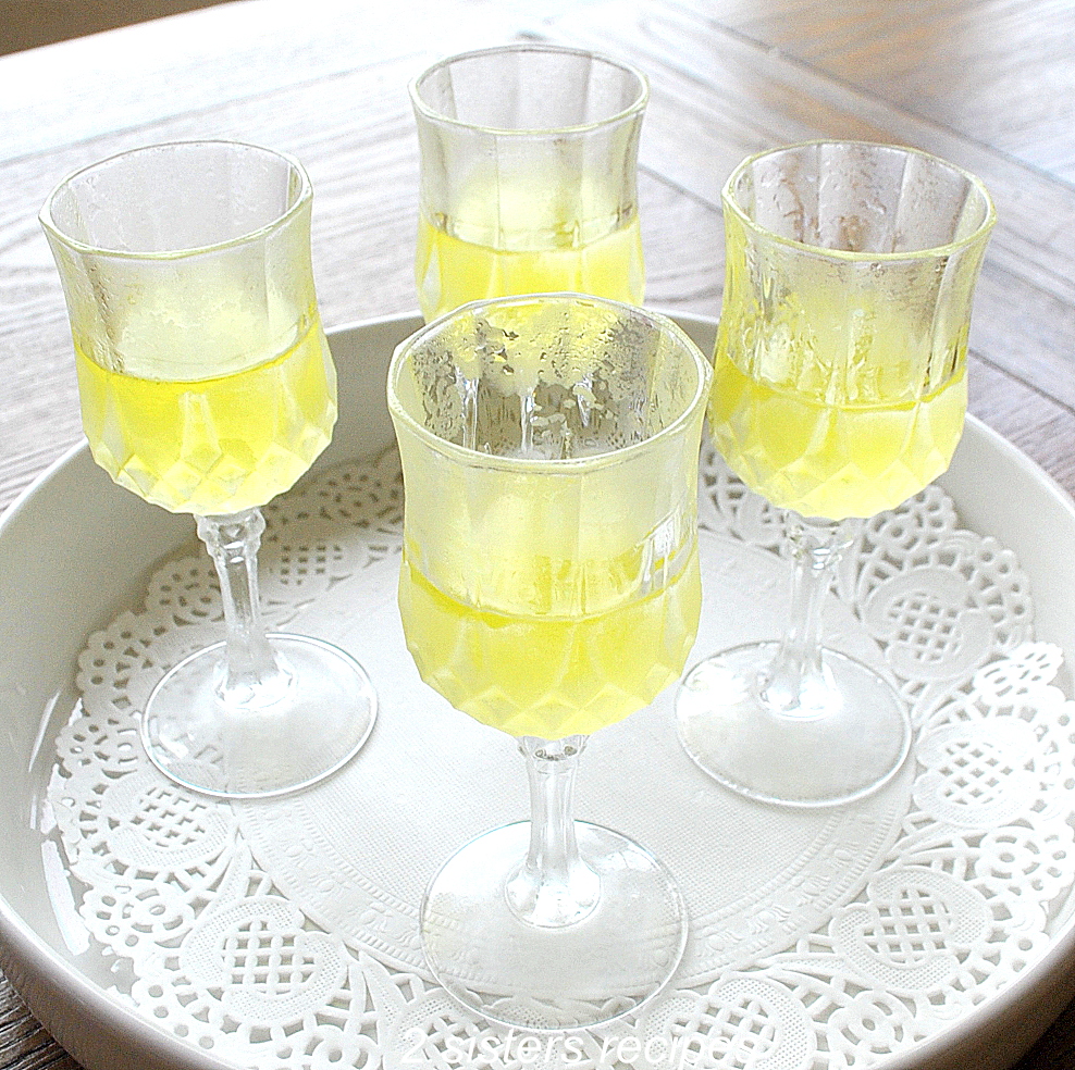 White plate with 4 cordial glasses filled with lemon liqueur in it. by 2sistersrecipes.com