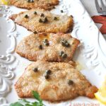 Four pieces of cooked veal with capers on top served on a white platter.