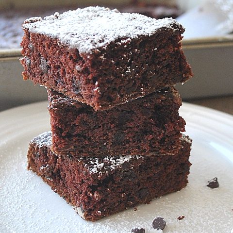 3 square brownies on top of once another on a white plate.