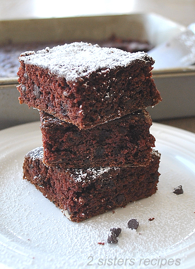3 square brownies on top of once another on a white plate.